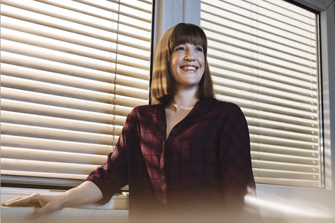 Porträt einer lächelnden Frau vor einem Fenster, lizenzfreies Stockfoto