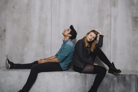 Young couple sitting in front of concrete wall stock photo