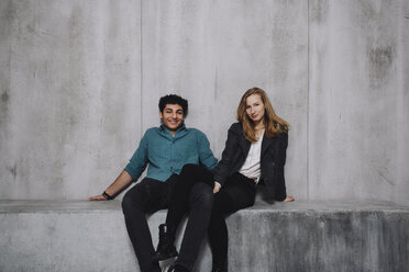 Young couple sitting in front of concrete wall, smiling - GCF000212