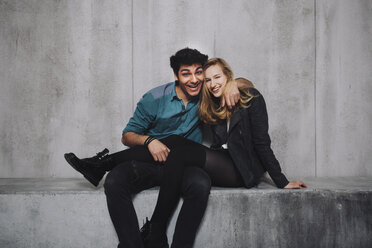 Young couple sitting in front of concrete wall, laughing - GCF000214