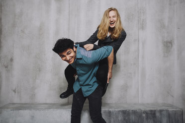 Young couple sitting in front of concrete wall, piggyback - GCF000218