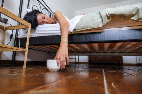 Frau im Bett, müde, Hand auf Kaffeetasse, lizenzfreies Stockfoto