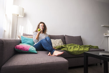 Portrait of smiling woman relaxing on couch eating an apple - SIPF000690