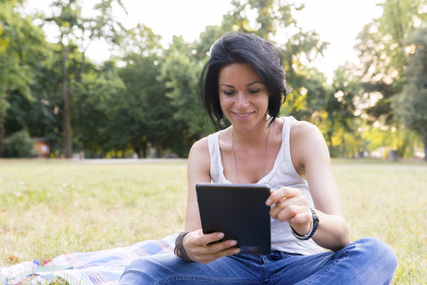 Lächelnde Frau, die auf einer Wiese sitzt und ein Tablet benutzt, lizenzfreies Stockfoto