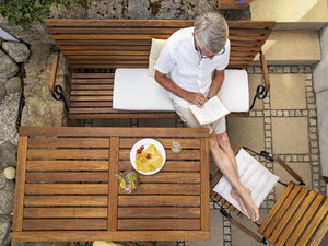 Senior man sitting on terrace reading book - LAF001705