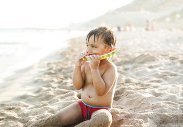 Little boy sitting on the beach at seafront eating watermelon - VABF000703