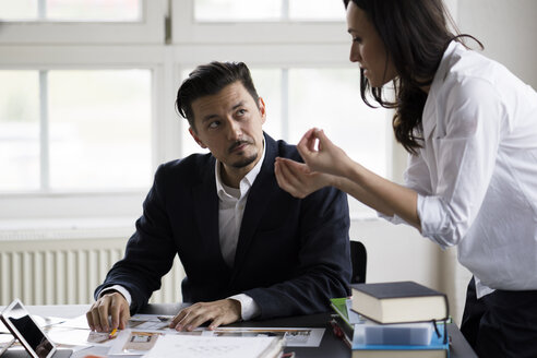 Businessman and woman sitting at desk in office, working together - FKF001897