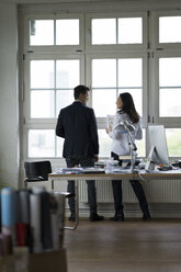 Businessman and woman standing at office window, disussing - FKF001898