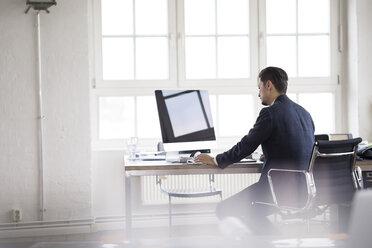 Businessman sitting in office, working on computer - FKF001899