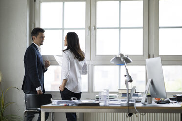 Businessman and woman standing at office window, disussing - FKF001901