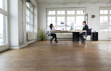 Geschäftsmann und Frau sitzen am Schreibtisch im Büro und arbeiten zusammen - FKF001916