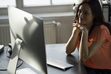 Businesswoman sitting in office, working on computer - FKF001919