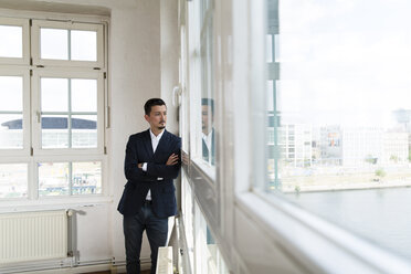 Businessman standing at the window with arms crossed - FKF001938