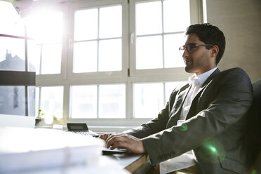 Businessman sitting in office, working on computer - FKF001942