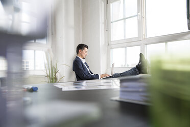 Businessman sitting with feet up and laptop on his lap - FKF001946