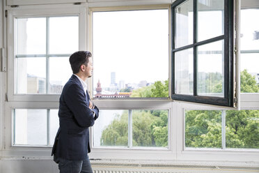 Businessman standing at open window with arms crossed - FKF001947