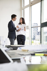 Businessman and woman standing at office window, disussing - FKF001956