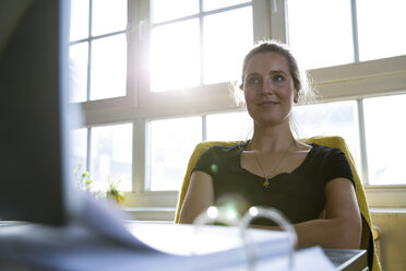 Woman sitting at desk with arms crossed - FKF001984