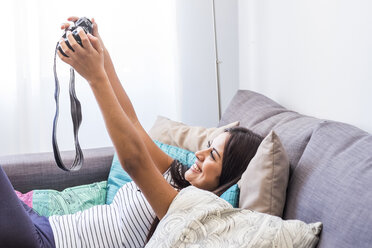 Glückliches Teenager-Mädchen liegt auf der Couch und macht ein Selfie mit der Kamera - SIPF000697
