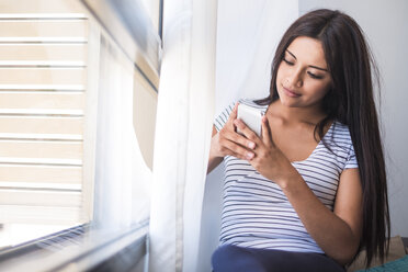 Teenager-Mädchen neben dem Fenster, das auf ein Handy schaut - SIPF000708