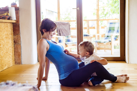 Schwangere Mutter spielt auf dem Boden mit ihrem kleinen Sohn, lizenzfreies Stockfoto