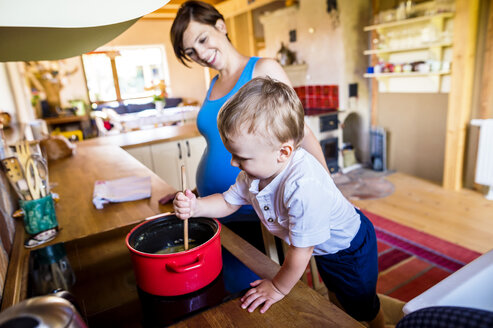 Kleiner Junge hilft seiner schwangeren Mutter beim Kochen, rührt im Topf - HAPF000603