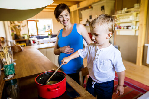 Kleiner Junge hilft seiner schwangeren Mutter beim Kochen, rührt im Topf - HAPF000604