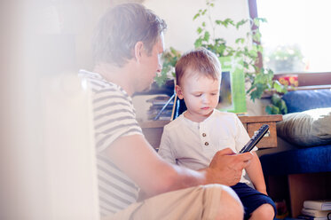 Father and son playing with remote control at home - HAPF000631