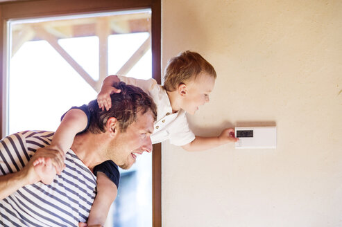 Vater trägt seinen Sohn auf den Schultern und stellt den Thermostat ein - HAPF000633