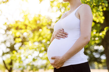 Pregnant woman holding belly, standing in nature - HAPF000636