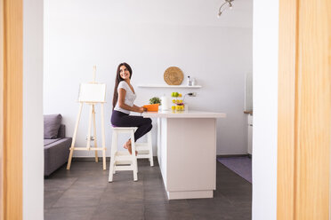 Smiling teenage girl with book sitting on a stool at home - SIPF000720