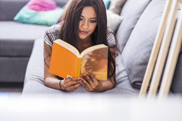 Teenage girl lying on the couch reading a book - SIPF000723