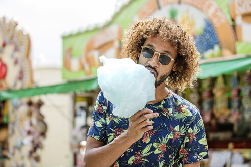 Young man eating candy floss at a fun fair - GD001082