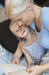 Mutter und kleine Tochter sitzen zusammen auf der Couch mit einem Buch - MIDF000761