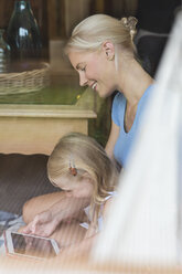 Mutter und kleine Tochter sitzen hinter einer Fensterscheibe und schauen gemeinsam auf eine Tafel - MIDF000762