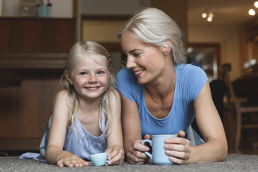 Mother and little daughter lying side by side on the floor holding cups - MIDF000765