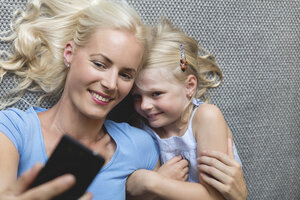 Mutter und ihre kleine Tochter liegen auf dem Boden und machen ein Selfie mit ihrem Smartphone - MIDF000767