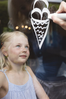 Portrait of little girl behind window pane watching her mother painting ice cream cone - MIDF000768