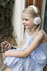 Lächelndes kleines Mädchen hört Musik mit Kopfhörern und Smartphone - MIDF000771