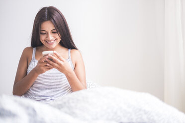 Teenage girl waking up, reading message on smartphone - SIPF000755