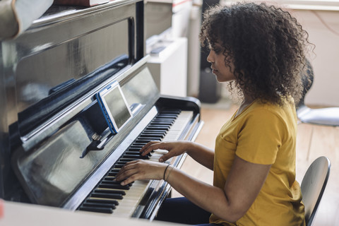 Junge Frau spielt Klavier und liest Noten von einem digitalen Tablet, lizenzfreies Stockfoto