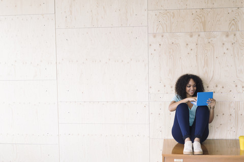 Junge Frau sitzt unter einem weißen Brett und benutzt einen Laptop, lizenzfreies Stockfoto