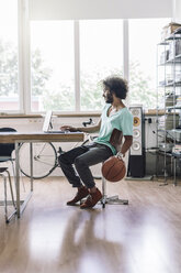 Junger Mann spielt mit Basketball im Büro - RIBF000448