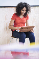 Junge Frau sitzt unter einem weißen Brett und benutzt einen Laptop - RIBF000449