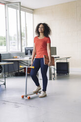 junge Frau trägt Laptop, benutzt Kickboard im Büro - RIBF000457