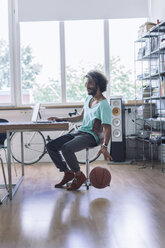 Young man playing with basketball in office - RIBF000471