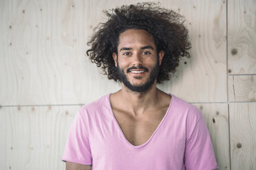 Young man leaning against wooden wall, smiling - RIBF000492