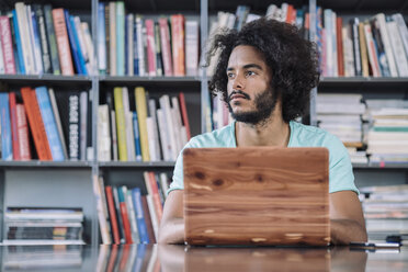 Junger Mann bei der Arbeit in einer Bibliothek, mit einem Holz-Laptop - RIBF000526