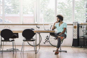 Junger Designer sitzt im Büro und benutzt einen Laptop - RIBF000529