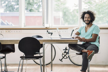 Junger Designer sitzt im Büro und benutzt einen Laptop - RIBF000530